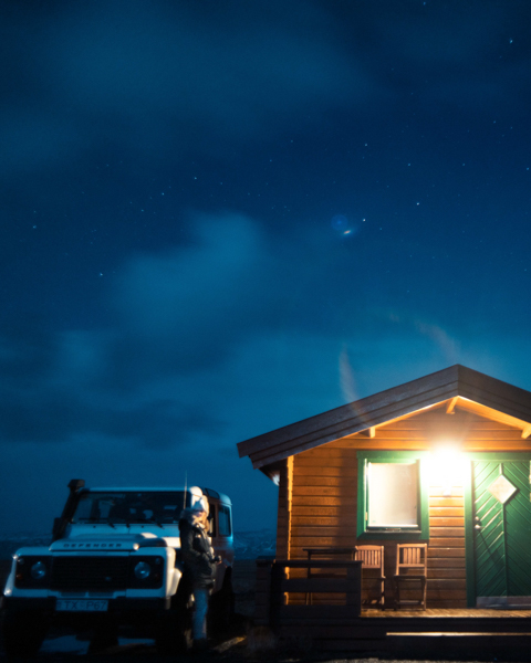 landrover Defender parked next to small wooden cabin at night in Iceland