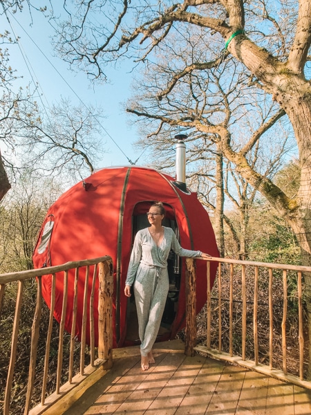 Girl in onesie pyjamas standing in front of hanging tree tent at Brook House Woods
