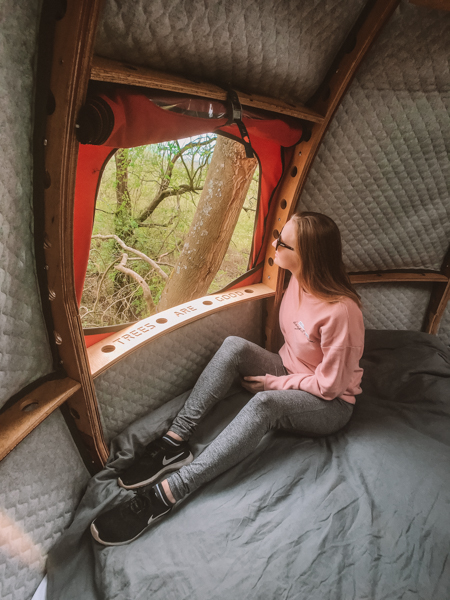 Girl sitting on bed looking out window in a tent in the woods