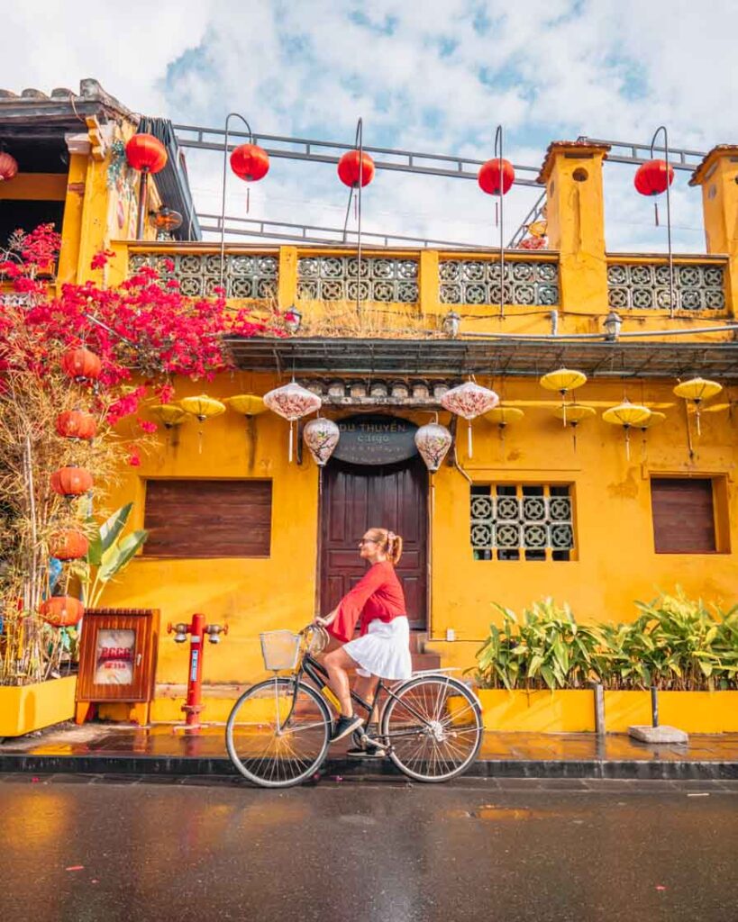 Girl riding bike in front of store and lanterns in Hoi An