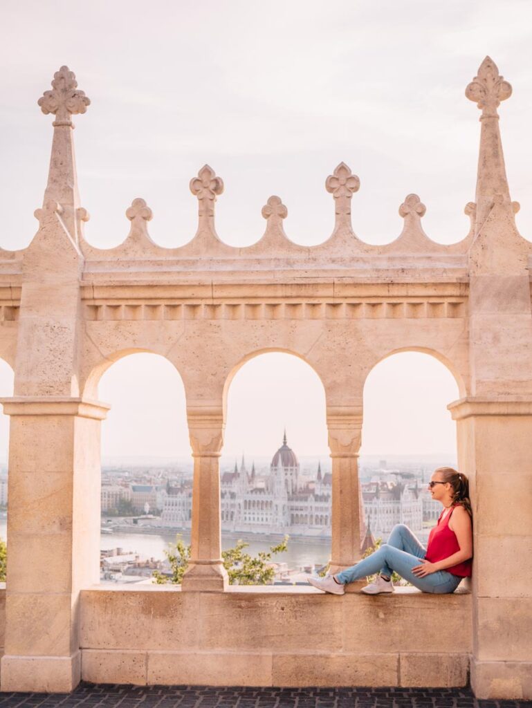 Girl sitting on ledge at Fisherman's Bastion in front of Hungarian Parliament building in Budapest