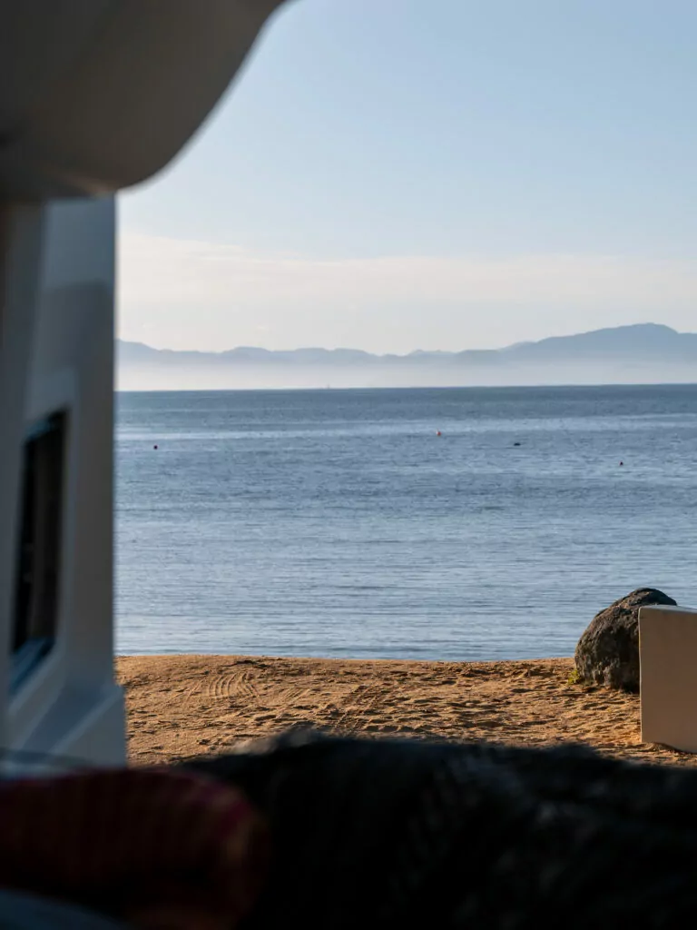 View of calm ocean waters and golden sand at Kaiteriteri Beach, seen from inside a campervan parked right on the shore