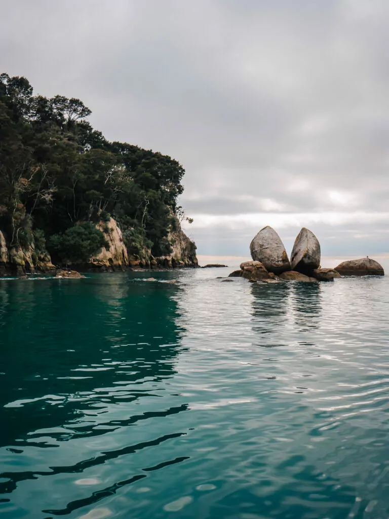 The iconic Split Apple Rock formation sits in shallow turquoise water off the coast of Abel Tasman National Park, with moody skies overhead