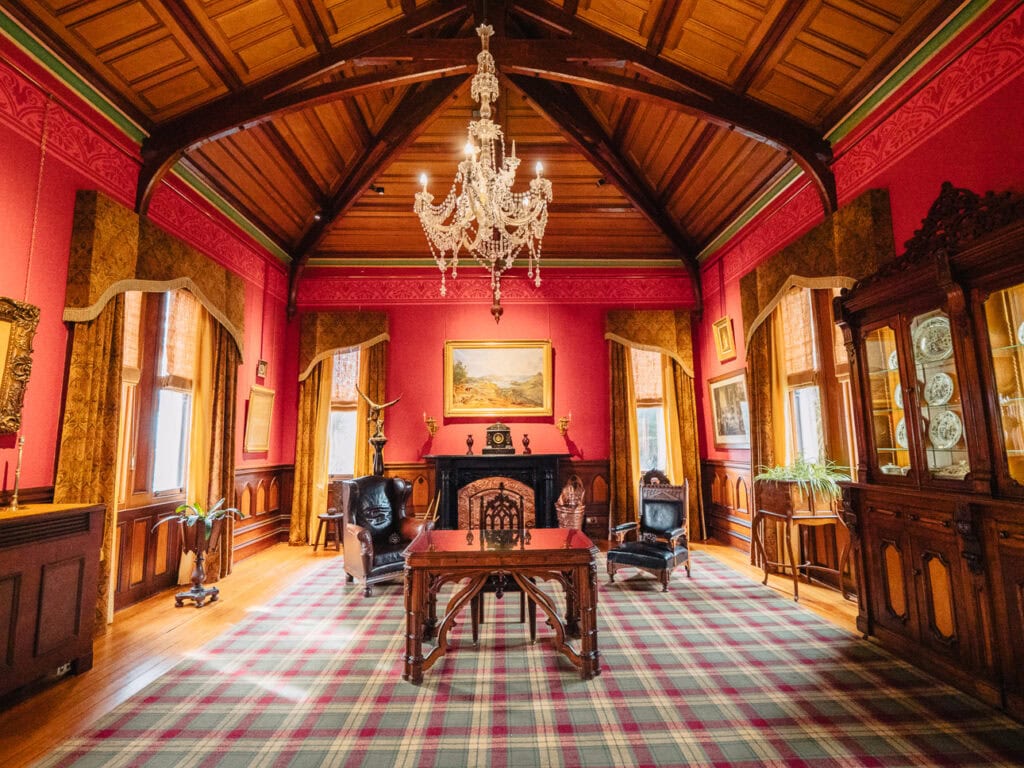 Elegant Victorian-era sitting room with red walls, ornate chandelier, antique furniture, fireplace and large windows at Larnach Castle near Dunedin