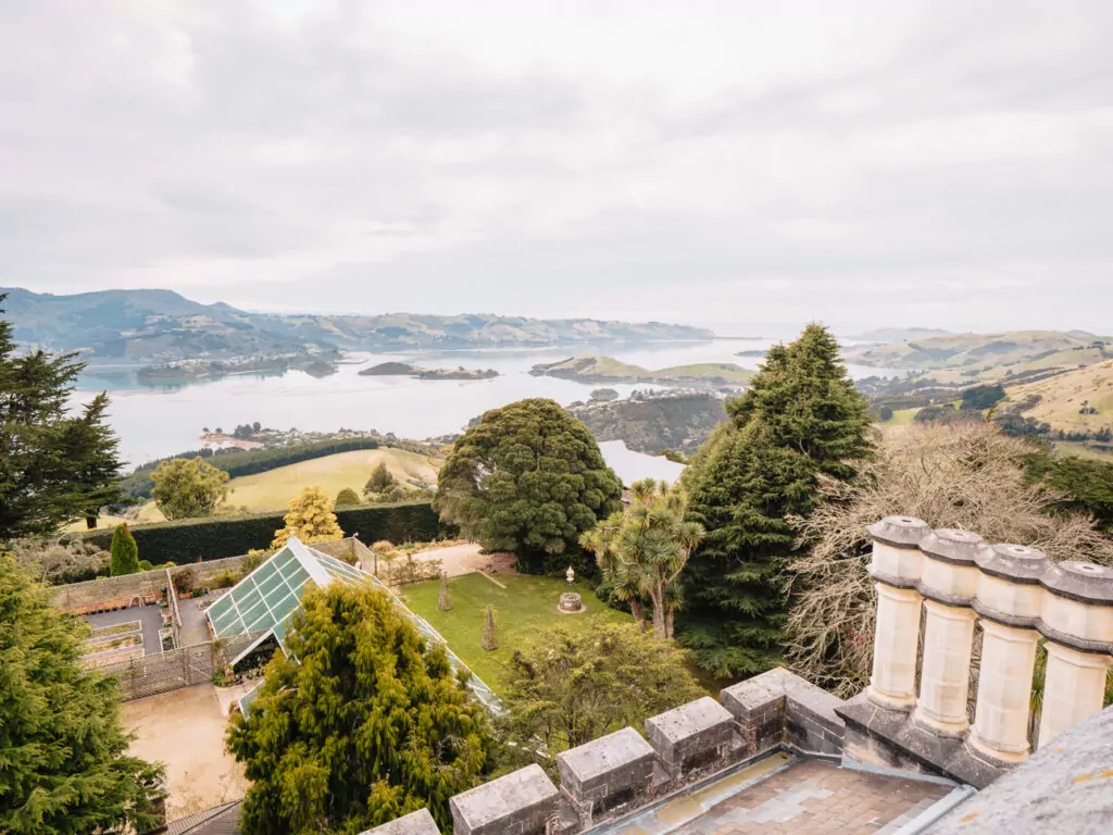 Panoramic view from Larnach Castle showing the harbour around Otago Peninsula under cloudy skies with native trees in foreground