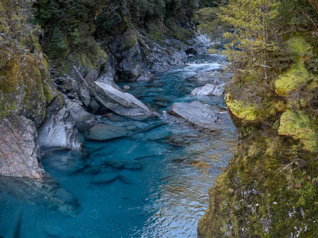 The crystal-clear Blue Pools near Haast Pass, where turquoise water flows between moss-covered rock walls in a forested alpine setting