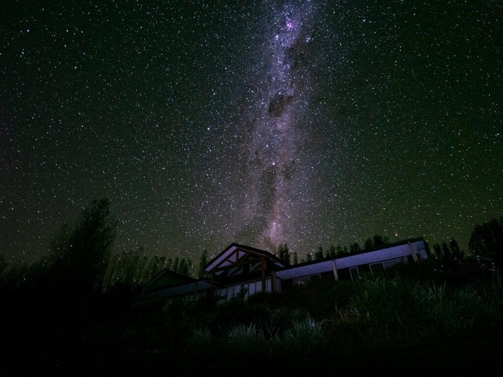 A starry night sky with the Milky Way clearly visible above a silhouette of Amuri Estate luxury lodge in Hanmer Springs
