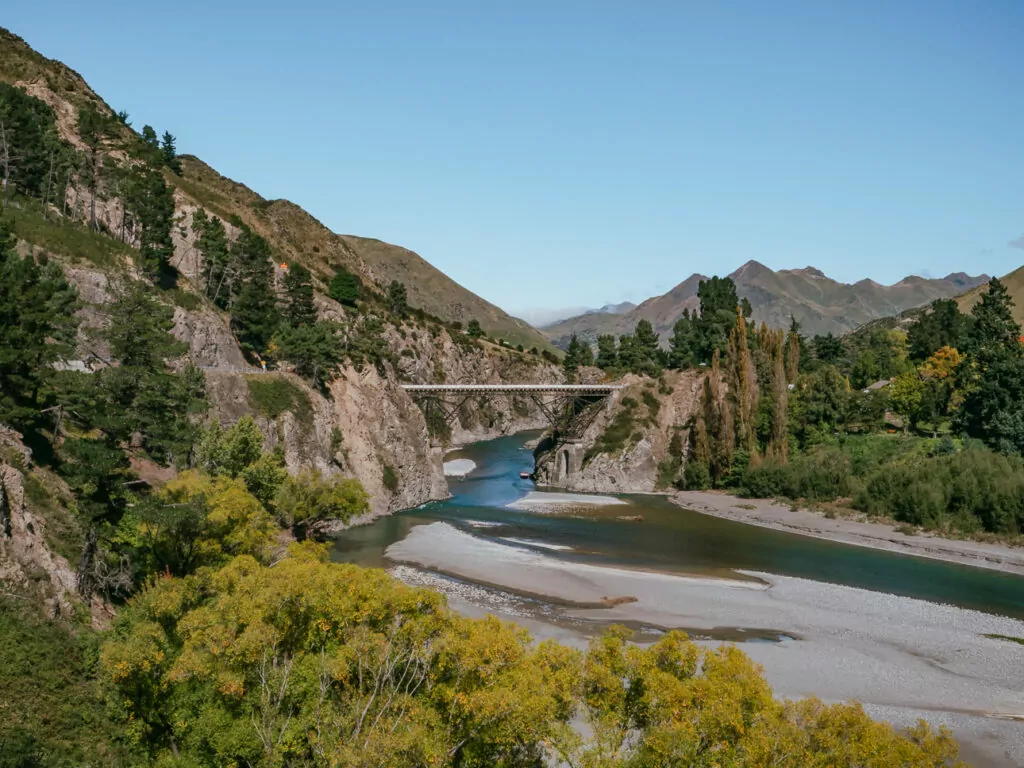 A high bridge spans the turquoise waters of Waiau River in Hanmer Springs, surrounded by rocky cliffs and forested hills in Canterbury’s foothills
