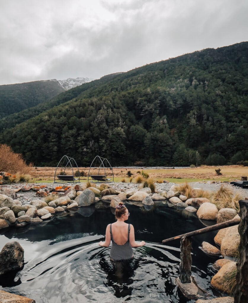 A woman relaxes in a natural hot pool at Maruia Hot Springs, surrounded by rocks and alpine scenery in New Zealand’s Southern Alps