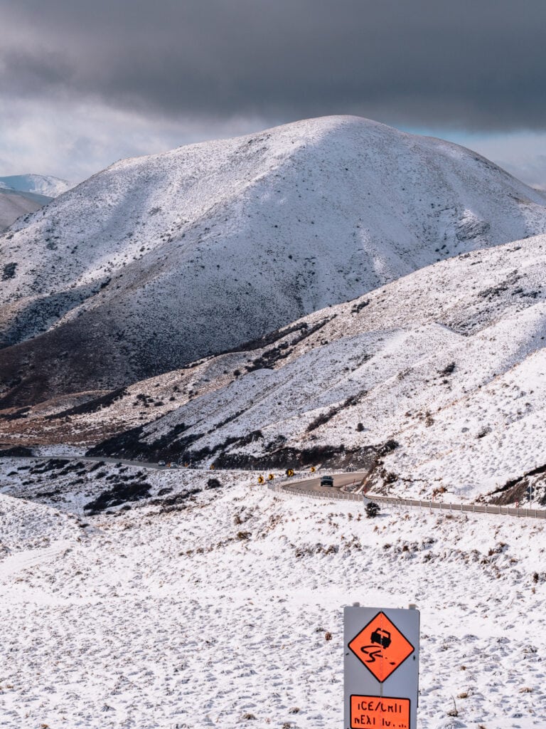 Snow-covered alpine landscape and winding road sign on the spectacular Lindis Pass mountain crossing.