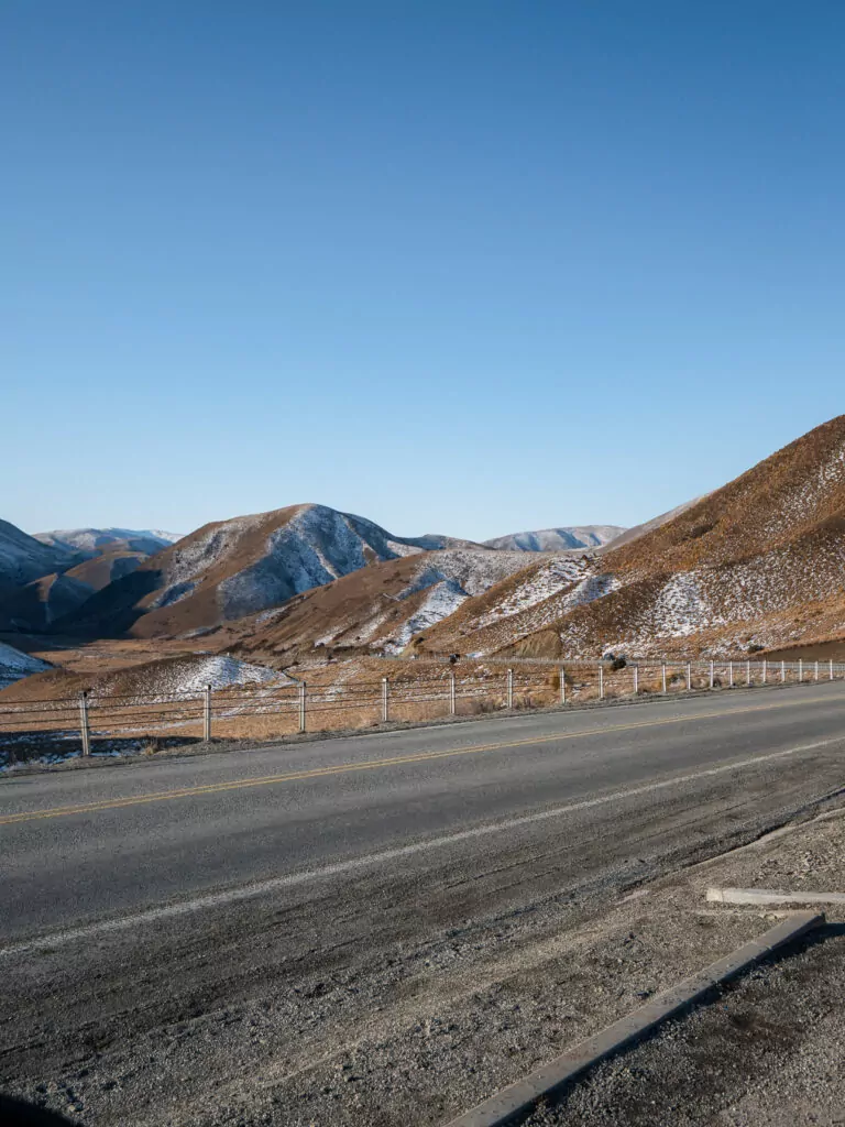 Open road driving through the arid, brown mountains of the Lindis Pass mountain crossing.