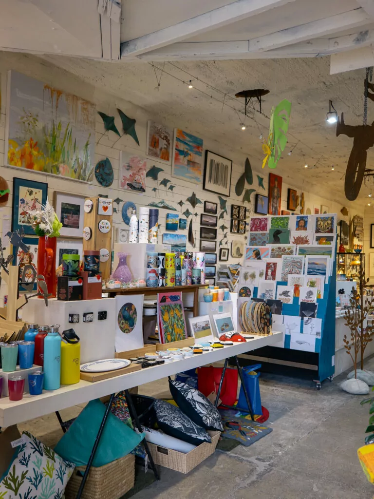 Inside a bright and eclectic art gallery at Mapua Wharf, filled with colourful local paintings, crafts, and handmade goods displayed on every wall and surface