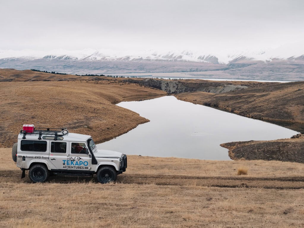 A Tekapo Adventures 4WD tour vehicle parked in the Cass Valley backcountry with snow-capped mountains behind