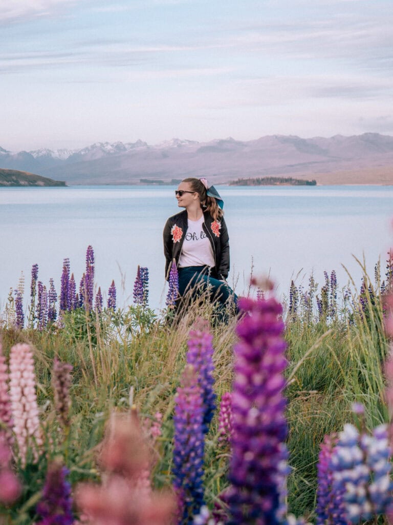 Alexx standing among blooming purple lupins on the shore of Lake Tekapo