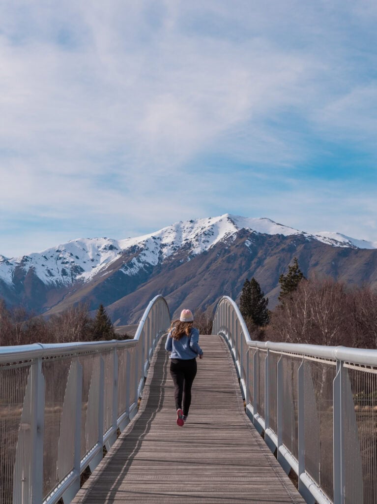Footbridge crossing the Tekapo River towards the Church of the Good Shepherd with a snow-capped mountain behind