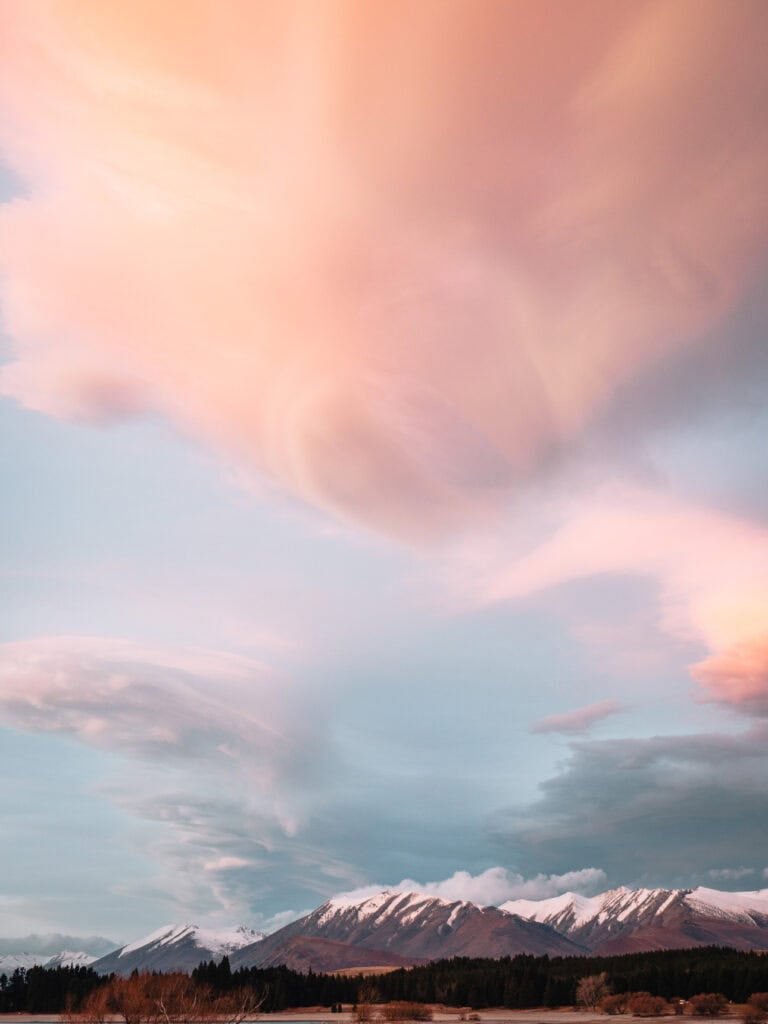 Dramatic pink and orange sunset clouds over Lake Tekapo with snowy mountains at the bottom of the frame
