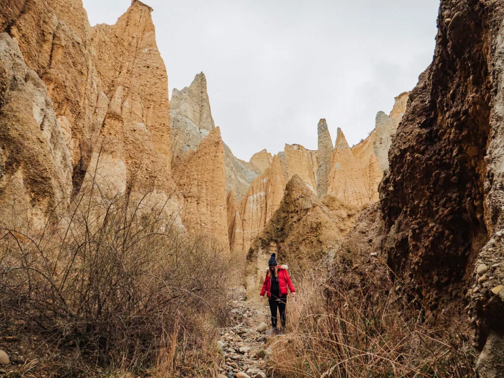 Hiker walking through the massive, rugged ochre clay pinnacles of the Omarama Clay Cliffs formation.