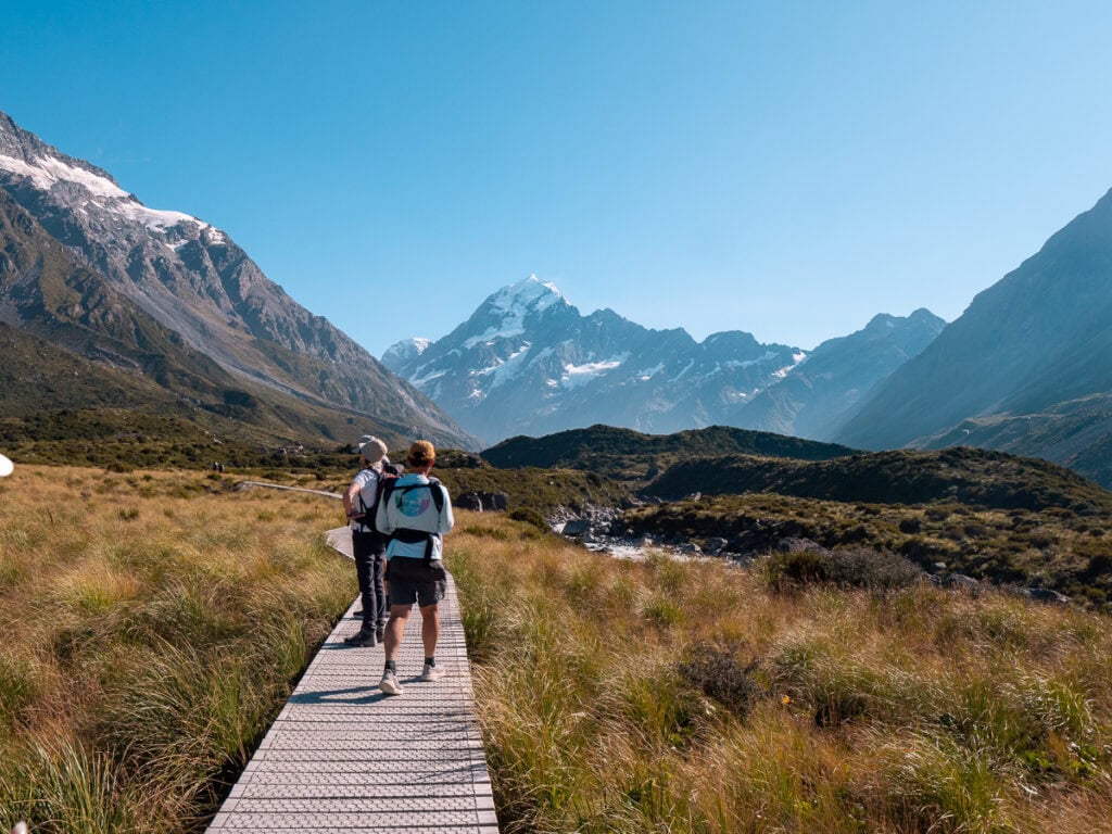 Hikers walking the boardwalk section of the Hooker Valley Track, one of the top activities near Tekapo, with mountains rising ahead