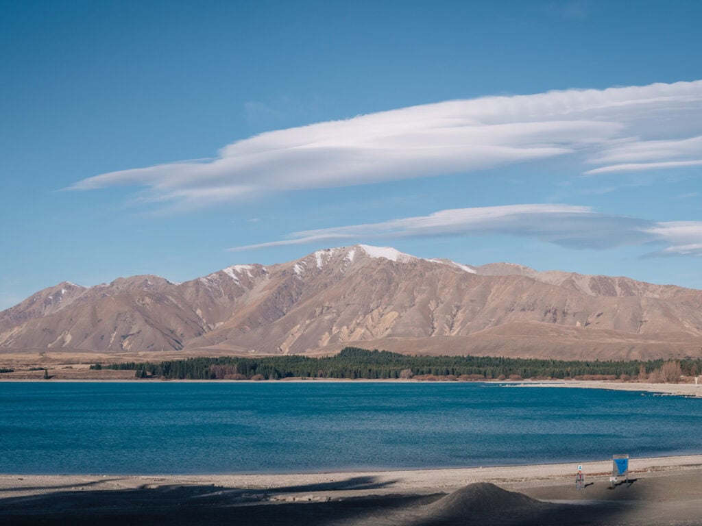 Calm Lake Tekapo in summer with soft clouds and mountains on the far shore