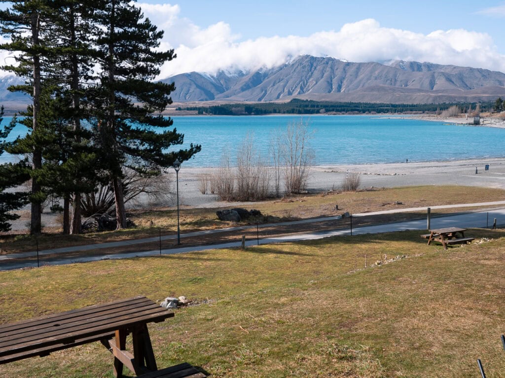 Picnic table under pine trees at Lakes Edge Holiday Park with views across Lake Tekapo to the mountains