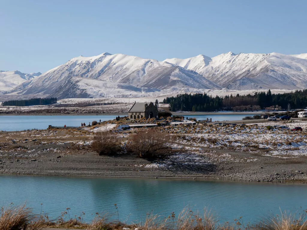 Iconic Church of the Good Shepherd stone chapel on the rocky shores of Lake Tekapo with snow-capped mountains of the Southern Alps behind