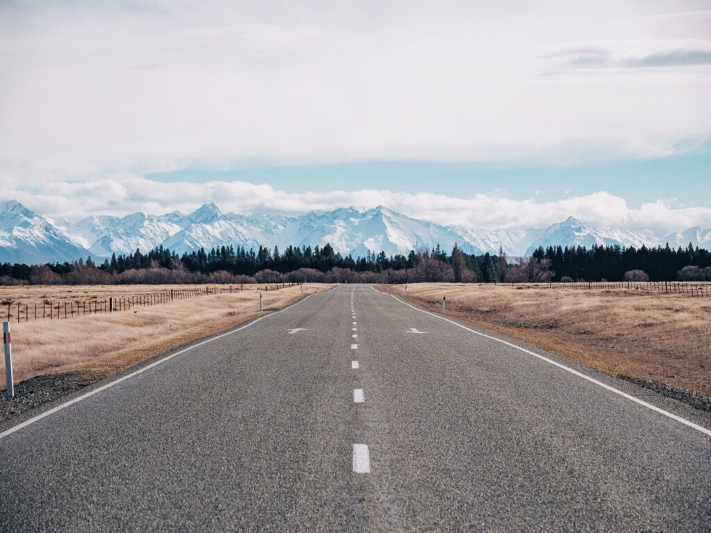 Long straight road heading into Tekapo with the snow-capped Southern Alps ahead