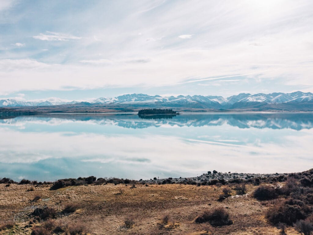 Motuariki Island sitting in the still mirror-like waters of Lake Tekapo/Takapō, viewed from Lilybank Road