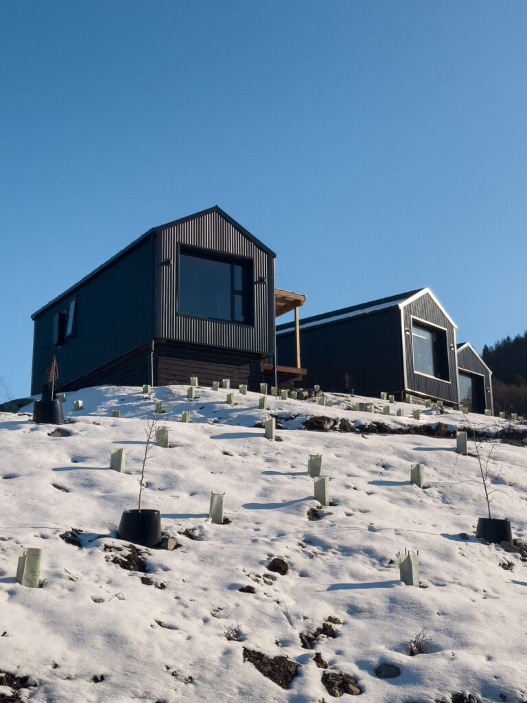 Modern black cabins at Lakes Edge Holiday Park overlooking a snowy Lake Tekapo
