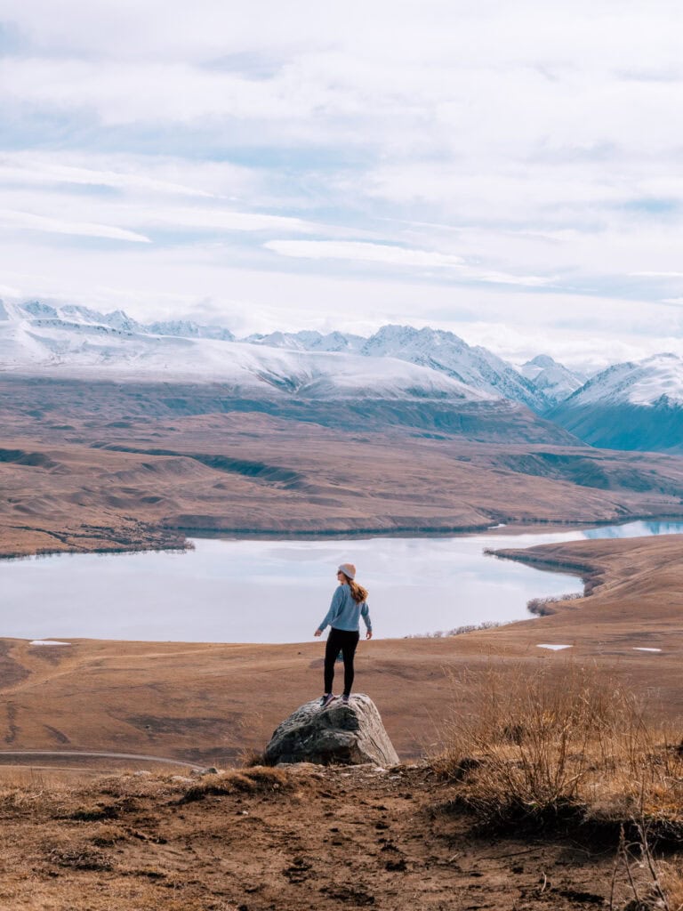 Alexx standing on a rocky outcrop looking over Lake Alexandrina from the Mount John summit near Tekapo