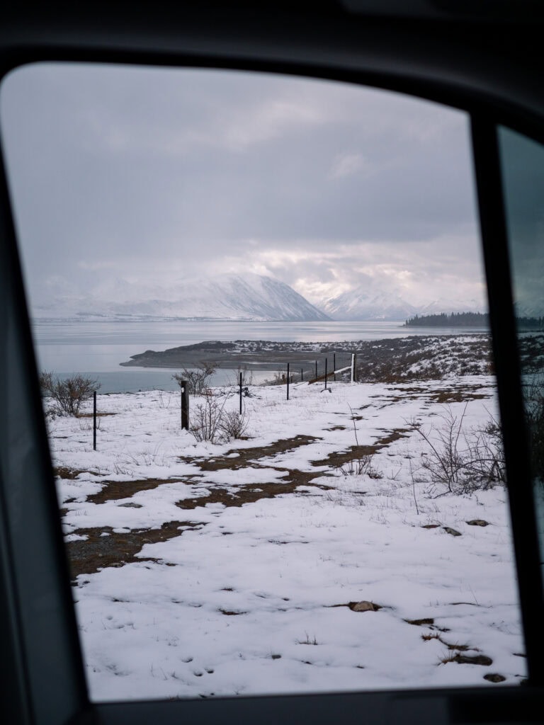 View from a campervan window of Lake Tekapo blanketed in snow