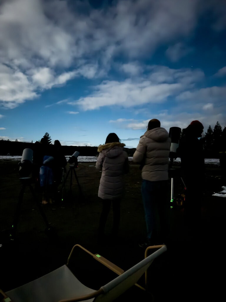 Stargazers bundled in winter jackets on the Chameleon Stargazing viewing platform under a full moon washed-out sky at Tekapo