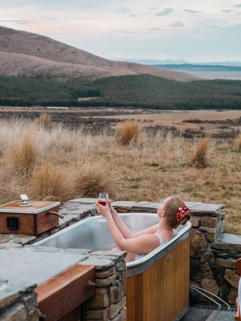 Alexx relaxing in the wood-fired outdoor hot tub at SkyScape cabin with Lake Pukaki in the distance