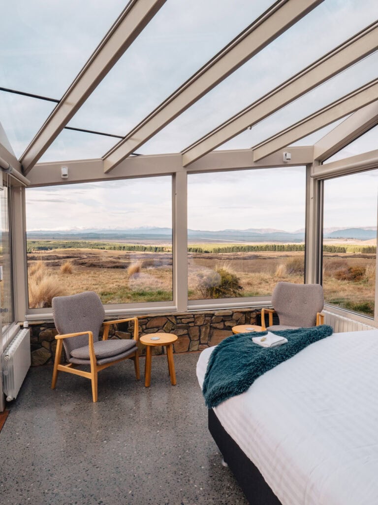 Interior of SkyScape glass cabin in Twizel with armchairs, a bed and panoramic views across the Mackenzie Basin