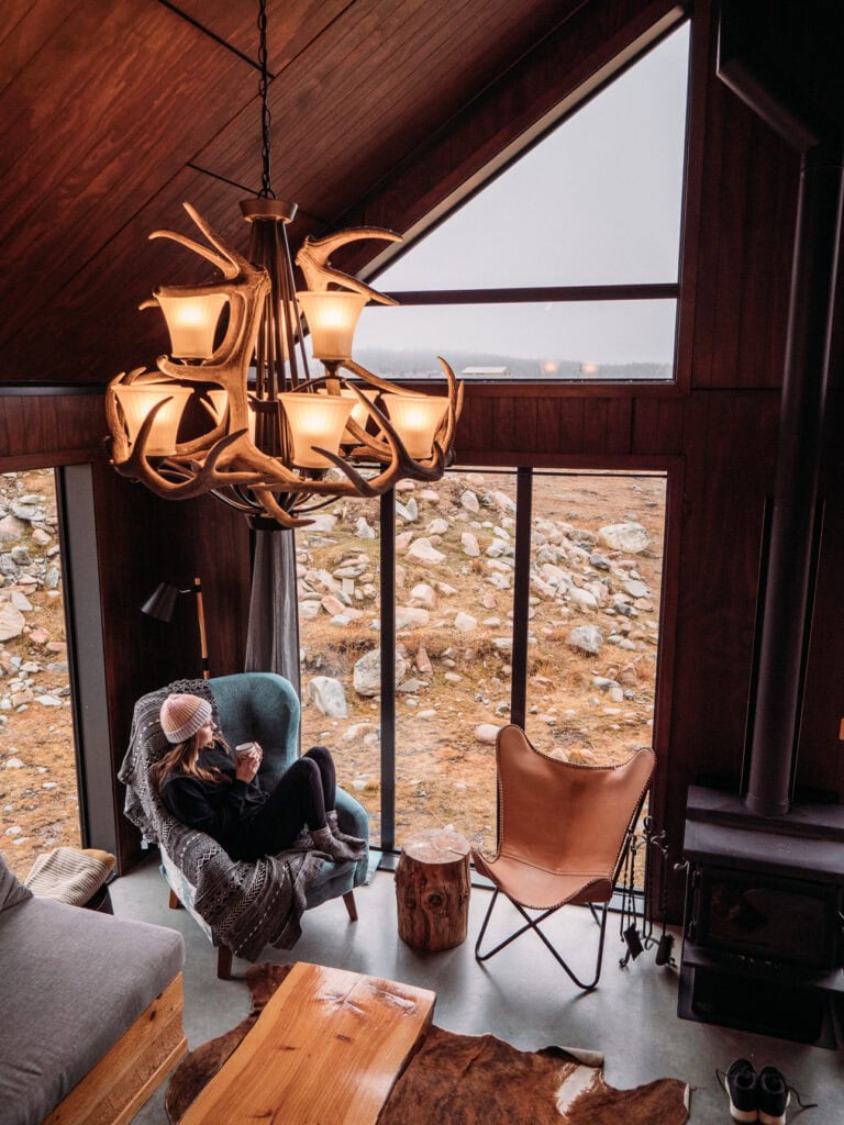 Cosy living area inside High Country Cabin in Twizel with antler chandelier and floor to ceiling windows overlooking the Mackenzie Basin