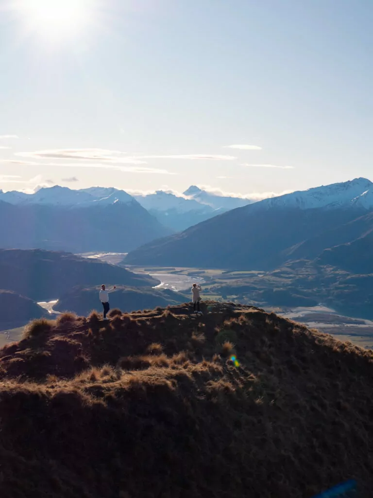 A group of travellers stands at the top of Coromandel Peak near Wānaka on a helicopter tour, with sweeping views of the Matukituki Valley and Southern Alps in the distance