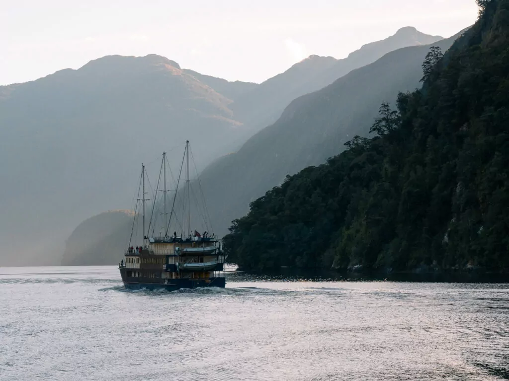 Tour boat cruising through the misty fjords of Doubtful Sound with steep forested cliffs lining both sides