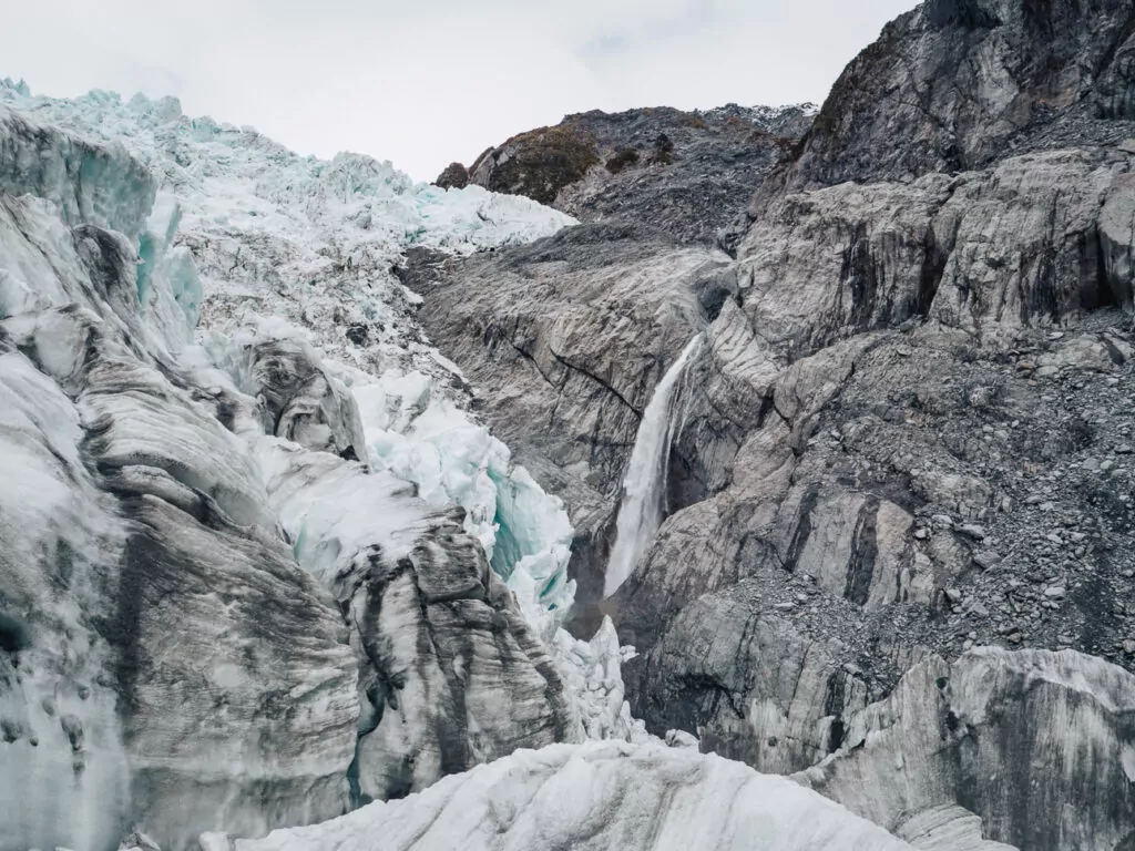 Jagged ice formations and narrow crevasses on Franz Josef Glacier with hikers exploring the glacier’s surface