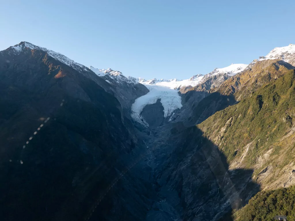 Aerial view of Franz Josef Glacier flowing through steep alpine valleys with snow-covered peaks