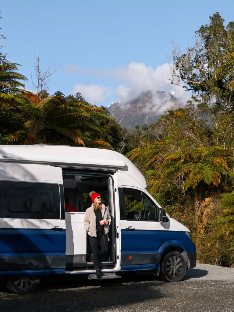 Person standing beside a campervan at Rainforest Retreat, surrounded by lush greenery and mist in Franz Josef