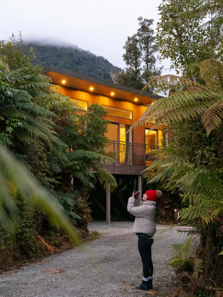 Wooden treehouse-style lodge lit up at dusk in the forest at Rainforest Retreat near Franz Josef