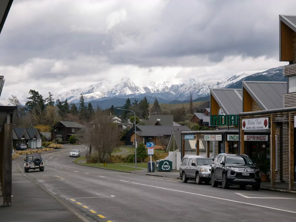 Snow-capped mountains behind the quaint main street of Hanmer Springs with alpine shops and parked cars