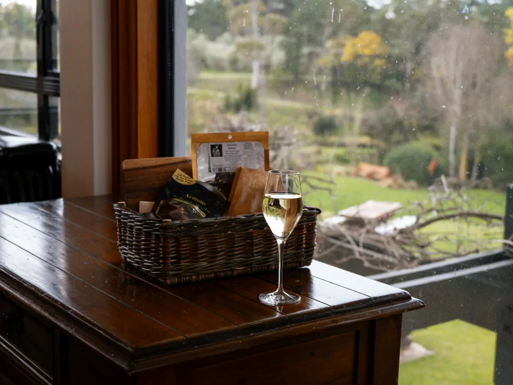 Glass of wine and gourmet picnic basket on a wooden table overlooking vineyard gardens at Pegasus Bay Winery