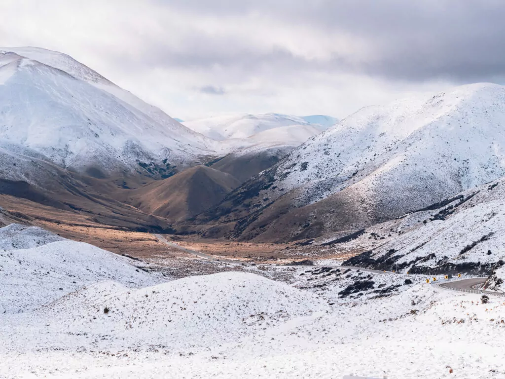 Snow-dusted ridgeline and winding alpine valley of Lindis Pass under cloudy skies