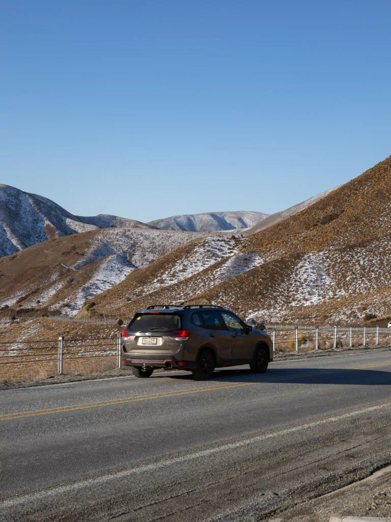 Car driving through the alpine tussock landscape of Lindis Pass on a clear winter day