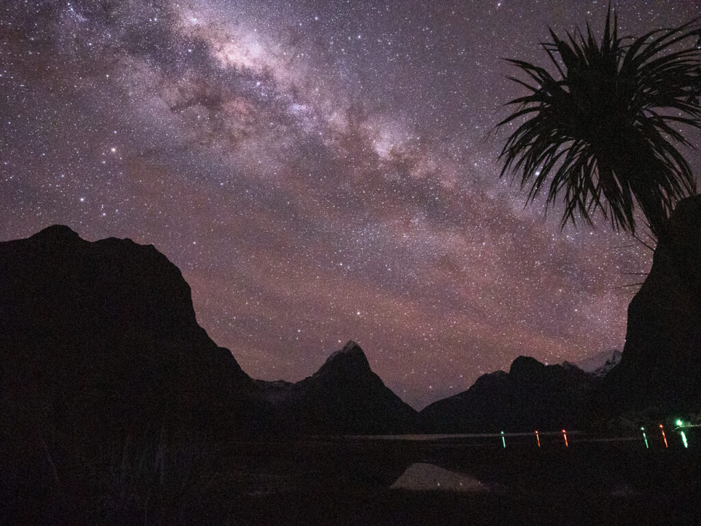 Starry sky and the Milky Way arching above silhouetted peaks at the Milford Sound foreshore