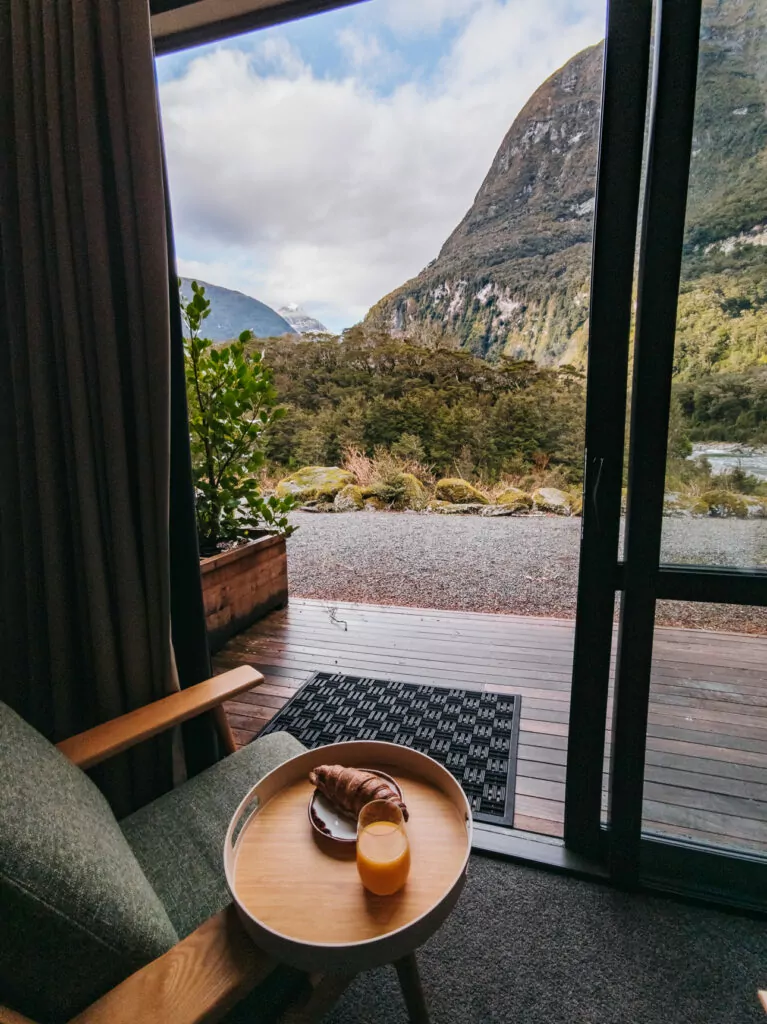 Coffee cup resting on a table beside an open glass door with a view of Milford Sound cliffs and native bush