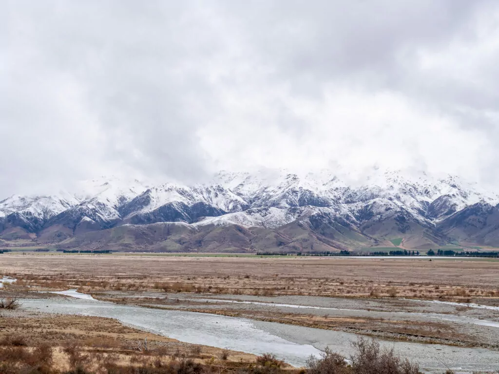 Expansive view across the Waitaki plains with braided rivers, golden fields, and snow-covered mountains