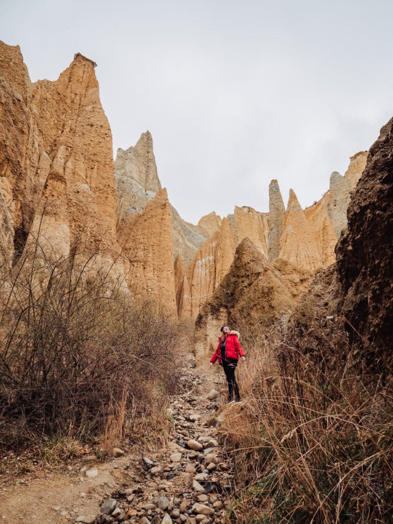 Hiker walking through the massive, rugged ochre clay pinnacles of the Omarama Clay Cliffs formation.