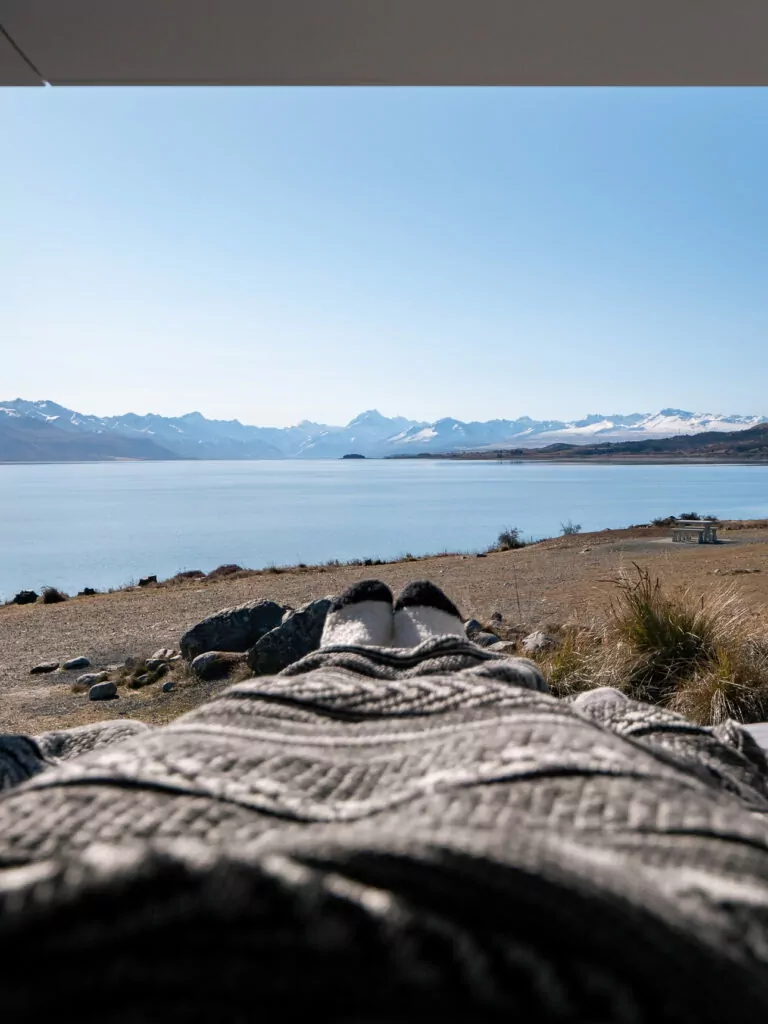 Blanket spread over a vanlifer's legs with a panoramic view over Lake Pukaki and the Southern Alps