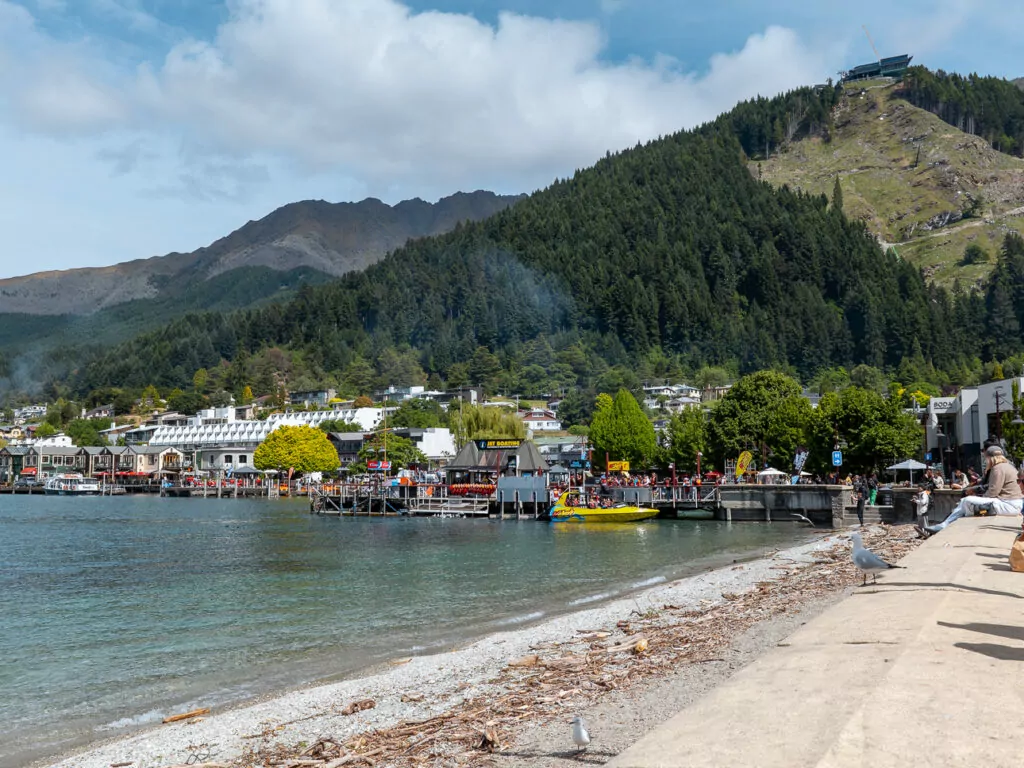 Row of vibrant buildings and restaurants along Queenstown’s waterfront on a partly cloudy day